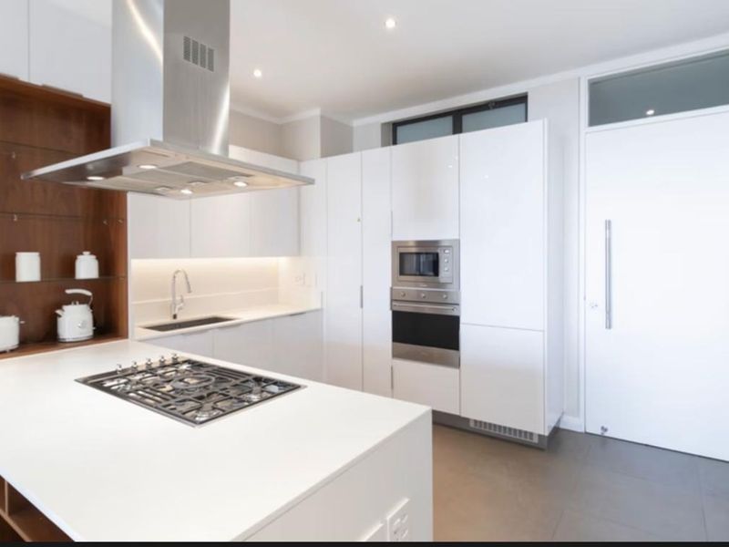 Modern kitchen featuring white cabinetry, stone countertops, integrated appliances including a gas hob, oven, and microwave, with sleek recessed lighting and tiled flooring.