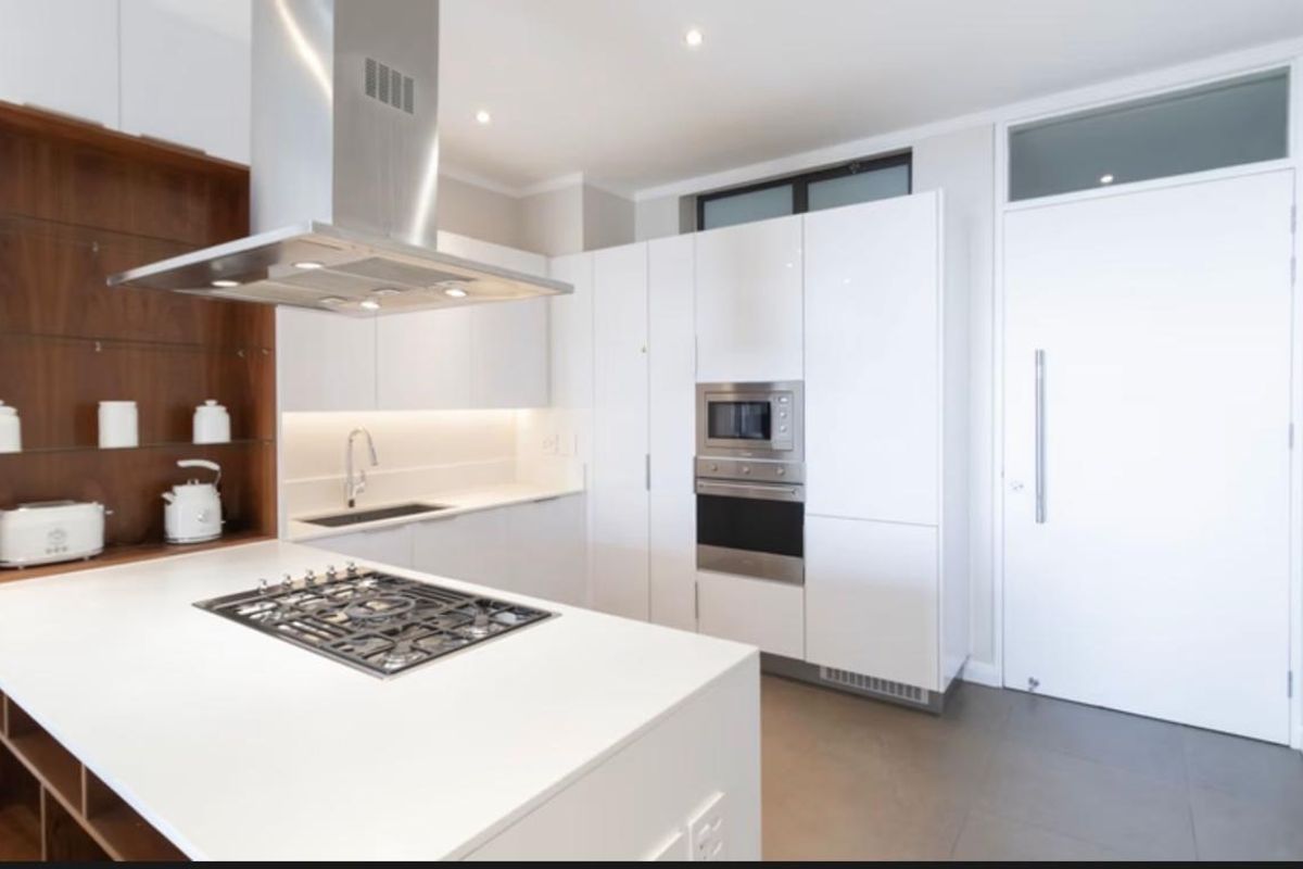 Modern kitchen featuring white cabinetry, stone countertops, integrated appliances including a gas hob, oven, and microwave, with sleek recessed lighting and tiled flooring.