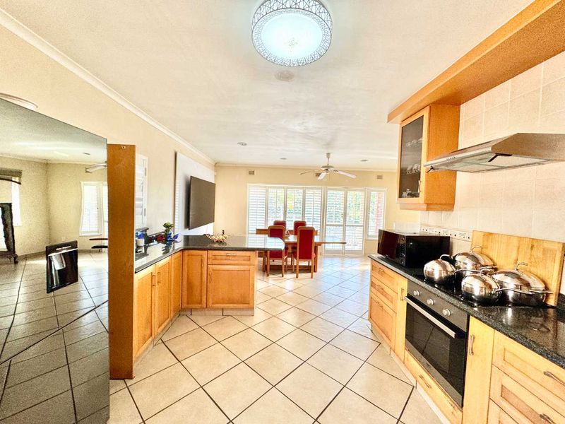 Open-plan kitchen and dining area featuring wooden cabinetry, granite countertops, tiled flooring, and plantation shutters, creating a functional and connected living space.
