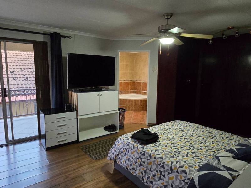 Spacious bedroom featuring laminate flooring, built-in cupboards, a ceiling fan, and a sliding door leading to a private balcony with en-suite bathroom access.