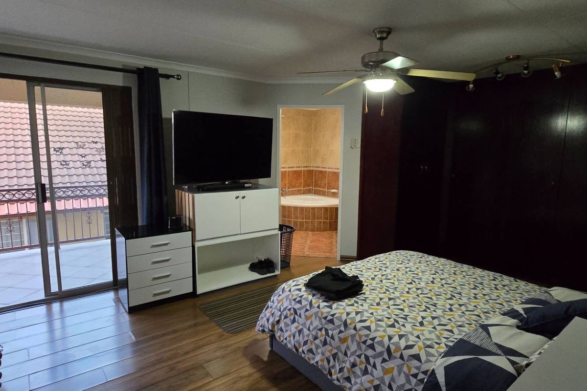 Spacious bedroom featuring laminate flooring, built-in cupboards, a ceiling fan, and a sliding door leading to a private balcony with en-suite bathroom access.