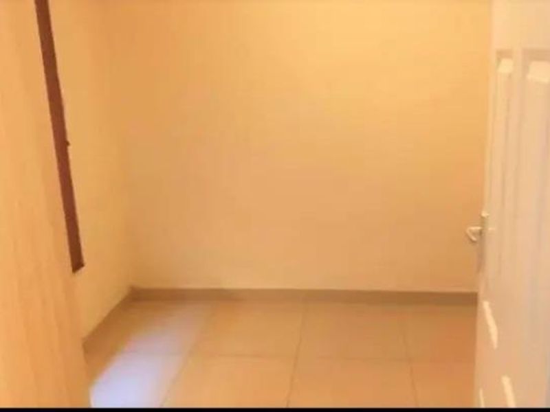 A vacant, neutrally painted bedroom featuring tiled flooring and a standard interior door.
