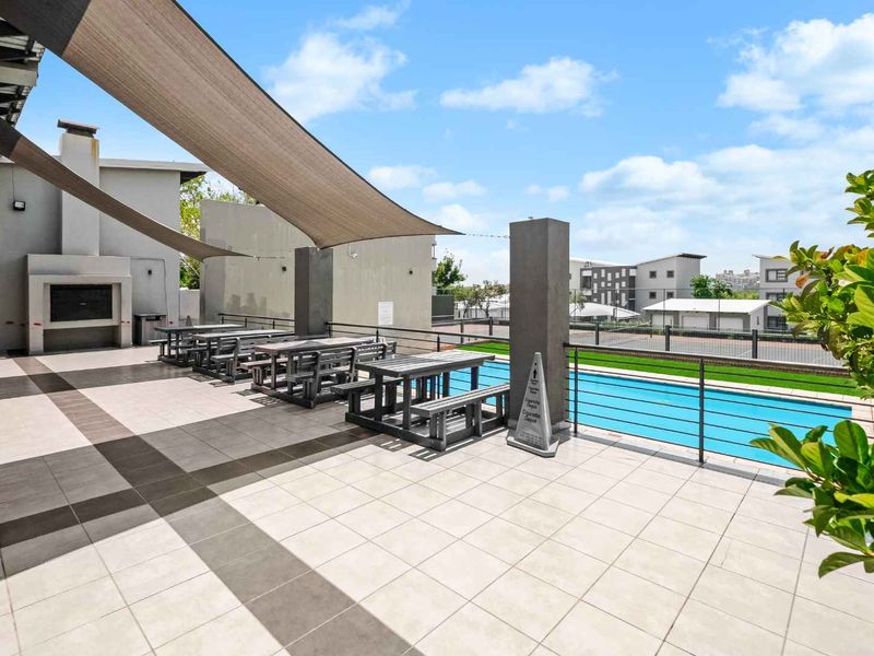 Outdoor pool area featuring a tiled patio, shade sail covering, and a built-in braai facility, ideal for communal recreation.