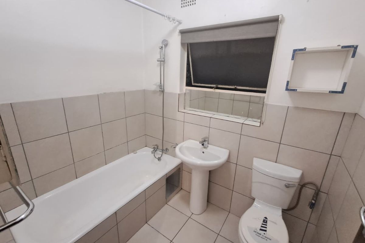 A functional bathroom featuring a standard bathtub with shower attachment, pedestal basin, and toilet, finished with neutral wall and floor tiling.