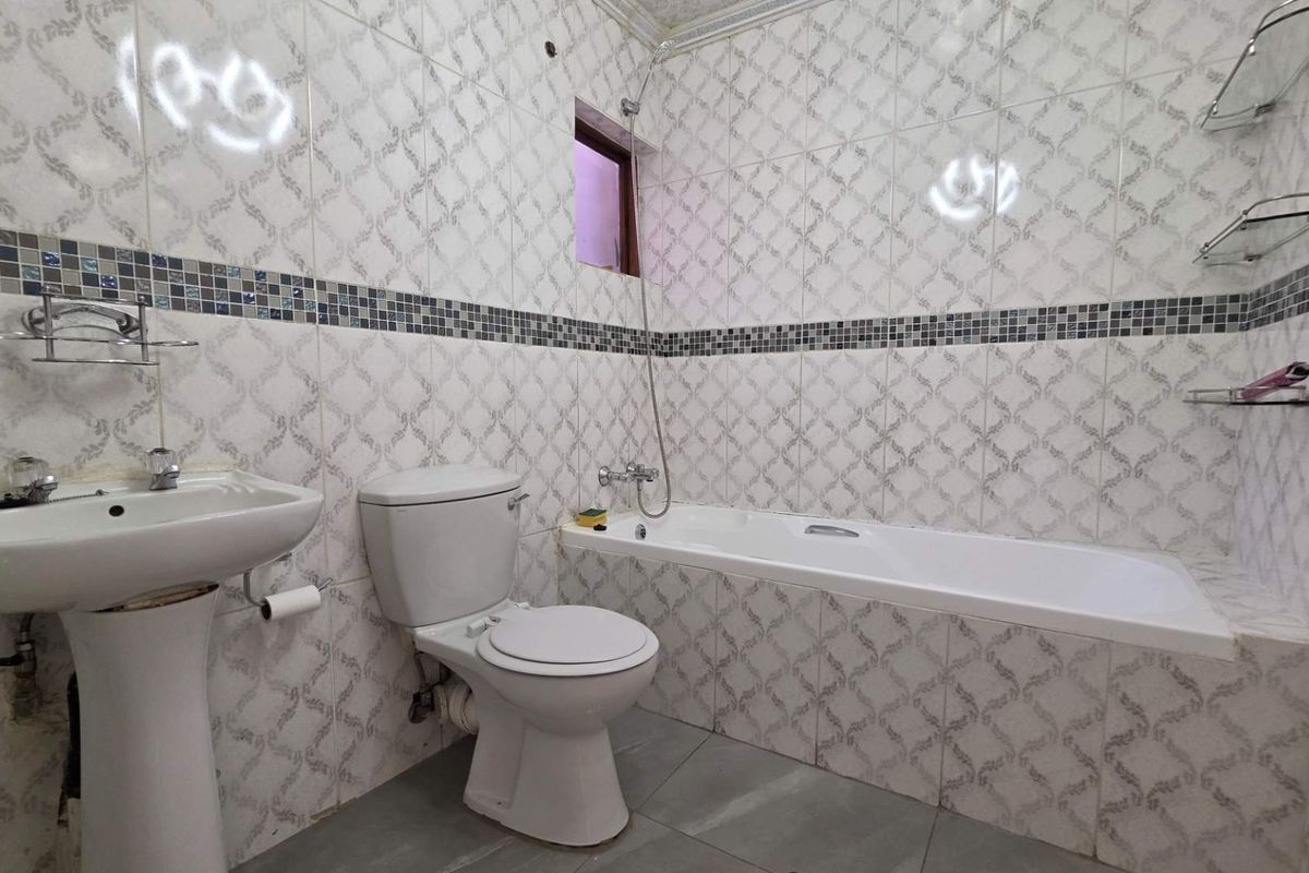 A functional bathroom featuring a pedestal sink, a standard bathtub with shower attachment, and full-height wall tiling with a decorative mosaic border.