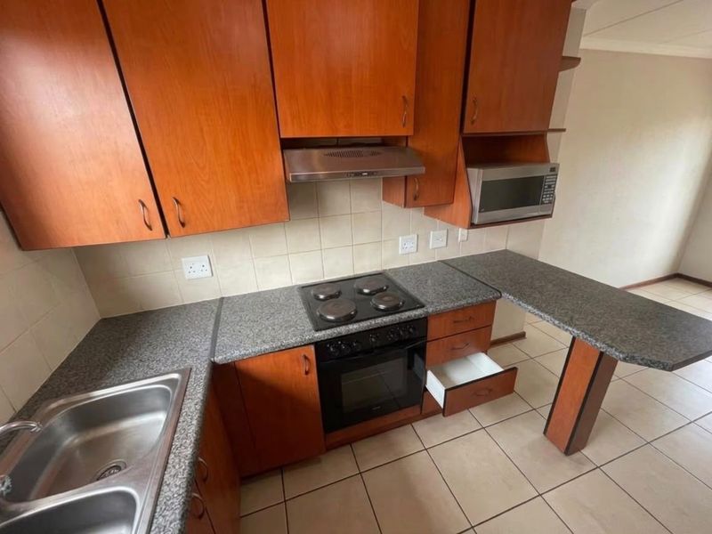 A functional kitchen featuring wooden cabinetry, granite countertops, built-in oven and hob, and a stainless steel double sink with tiled flooring.