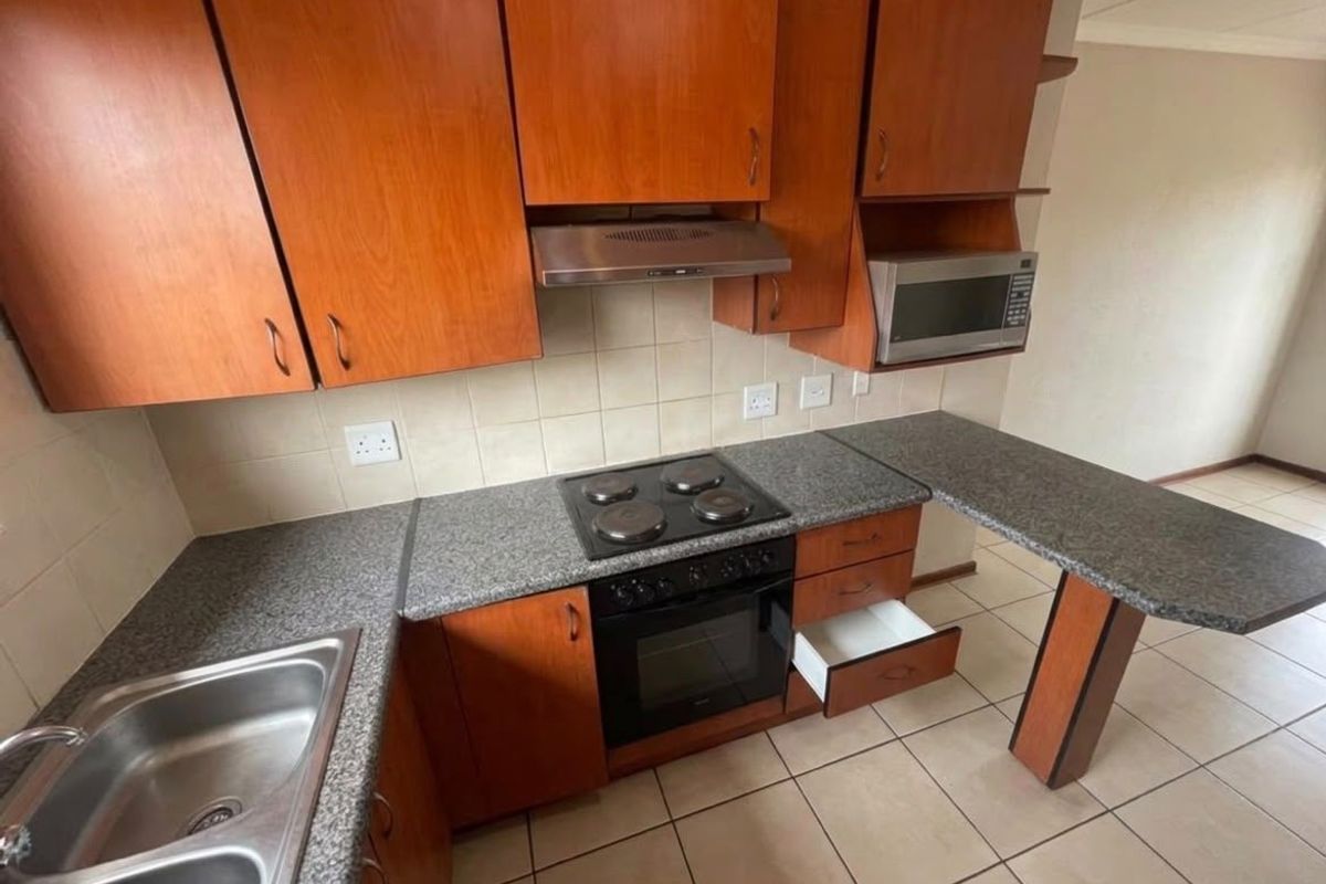 A functional kitchen featuring wooden cabinetry, granite countertops, built-in oven and hob, and a stainless steel double sink with tiled flooring.