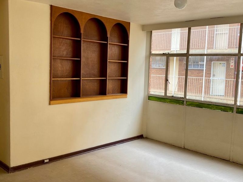 An empty living area featuring a built-in wooden arched shelving unit and large windows overlooking the exterior building facade.