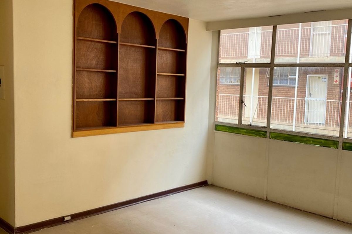 An empty living area featuring a built-in wooden arched shelving unit and large windows overlooking the exterior building facade.
