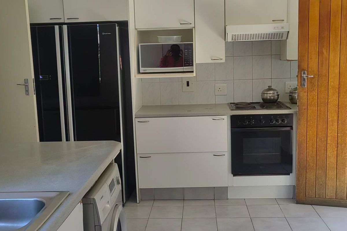 Functional kitchen featuring white cabinetry, built-in oven, hob, extractor fan, and tiled flooring with adjacent laundry area.