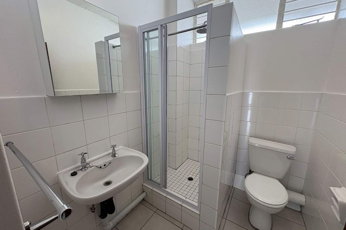 A functional bathroom featuring a walk-in shower enclosure, pedestal basin, and toilet with white wall tiling and neutral floor tiles.