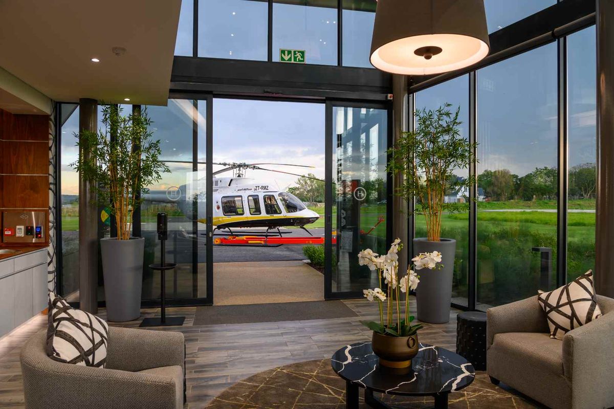 Modern lounge area featuring floor-to-ceiling glass walls with direct views of the helipad and surrounding landscape.