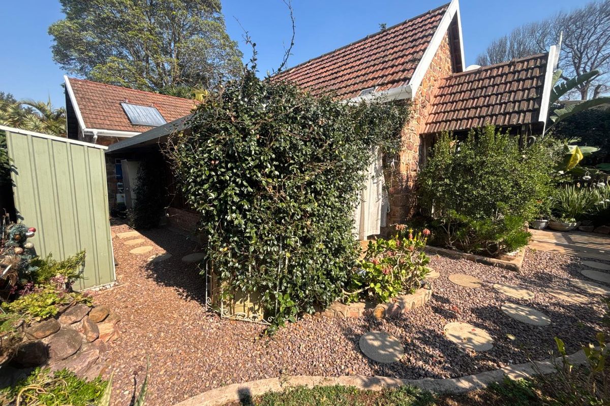 Rear exterior view of the townhouse featuring stone cladding, a tiled roof with solar heating, and a landscaped garden with gravel and stepping stones.