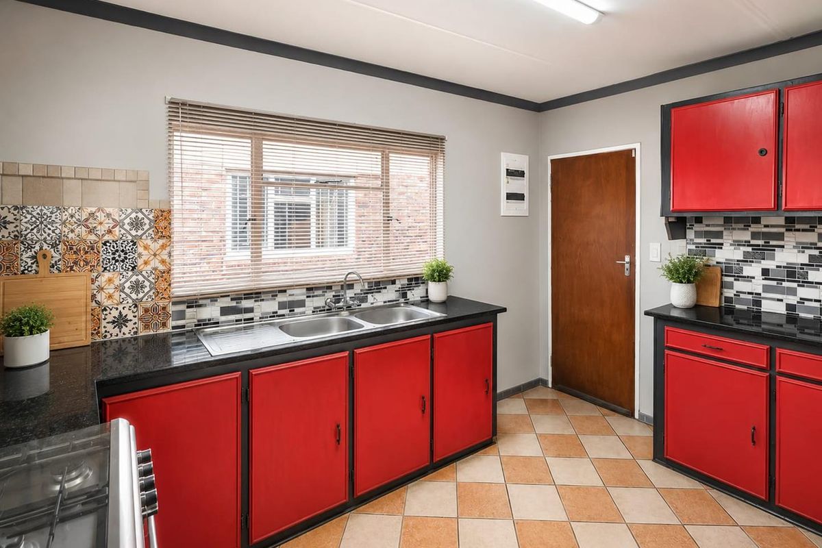 A functional kitchen featuring vibrant red cabinetry, black countertops, patterned tile backsplashes, and tiled flooring with a window overlooking the exterior.