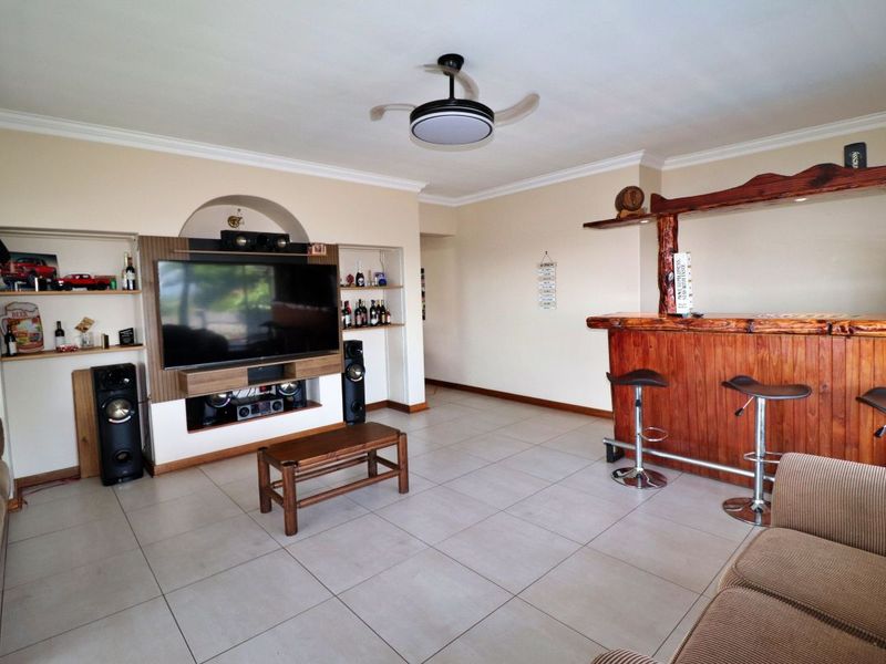 Spacious living area featuring a built-in wooden bar, custom media cabinetry, tiled flooring, and a ceiling fan, offering a comfortable entertainment space.