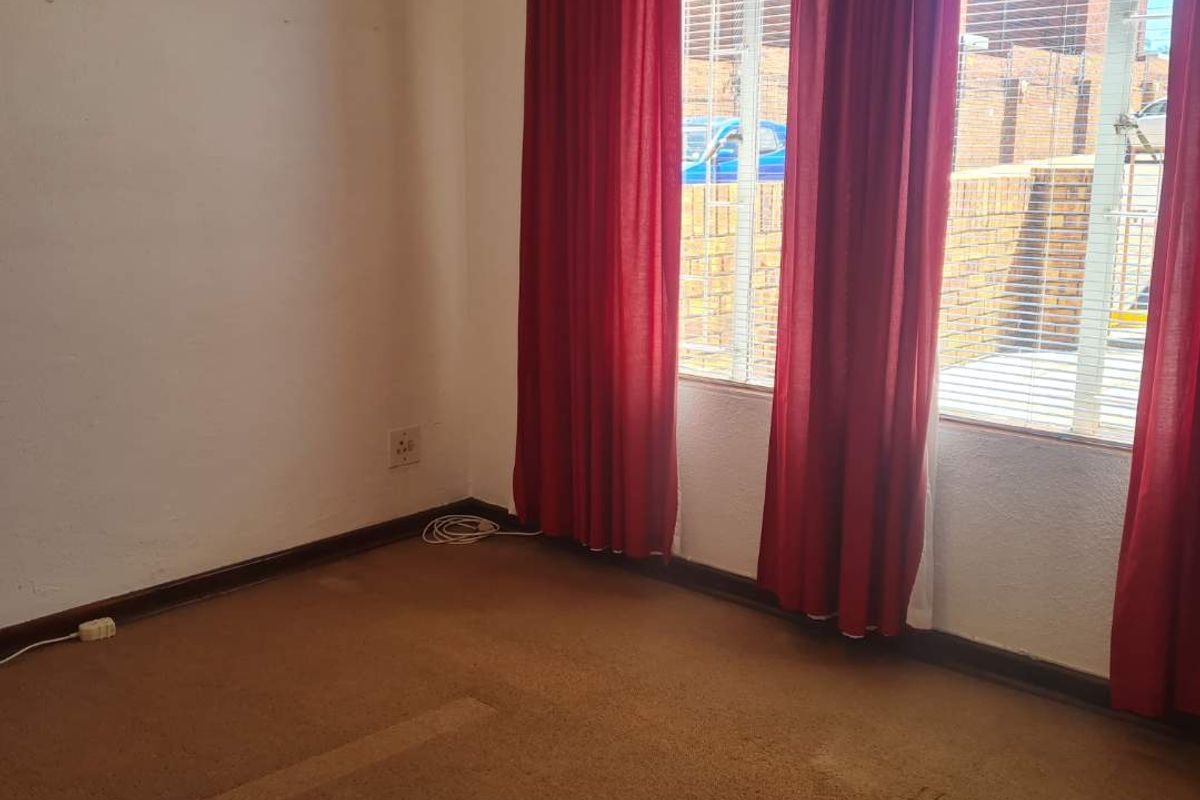 An empty bedroom featuring carpet flooring, window blinds, and natural light, presenting a blank canvas for potential renovation or restyling.