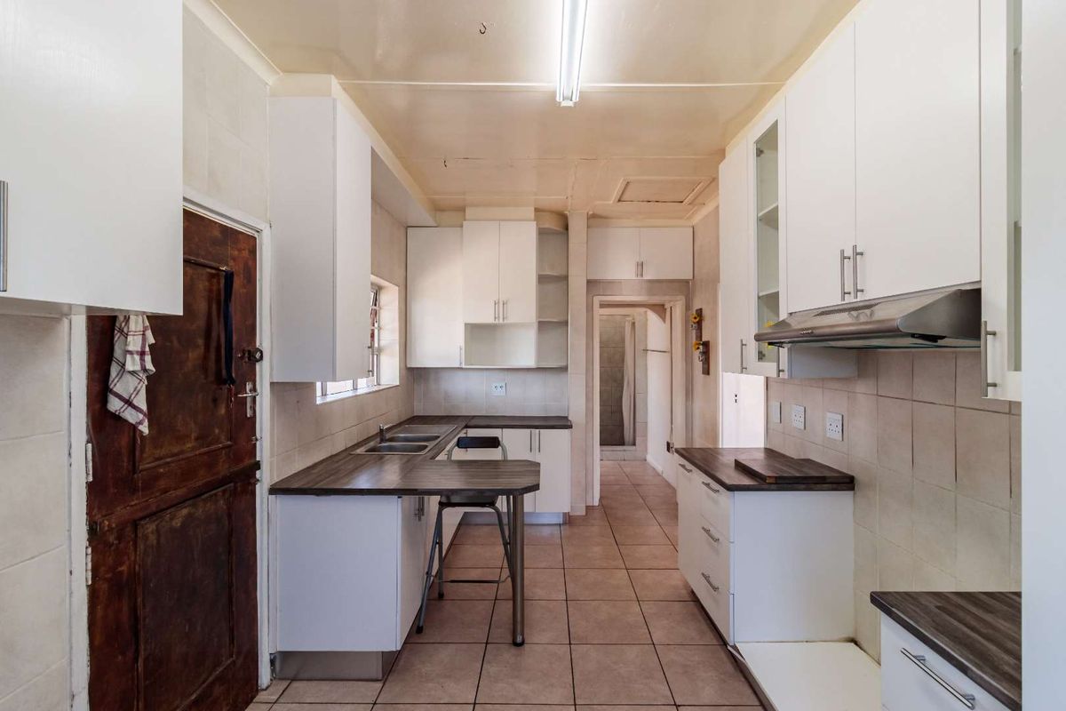 A functional kitchen featuring white built-in cabinetry, dark laminate countertops, tiled flooring, and an integrated extractor fan, offering a clean canvas for updates.