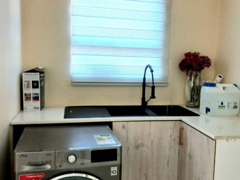 A functional laundry area featuring modern built-in cabinetry, a sleek undermount sink with a gooseneck faucet, and tiled flooring.
