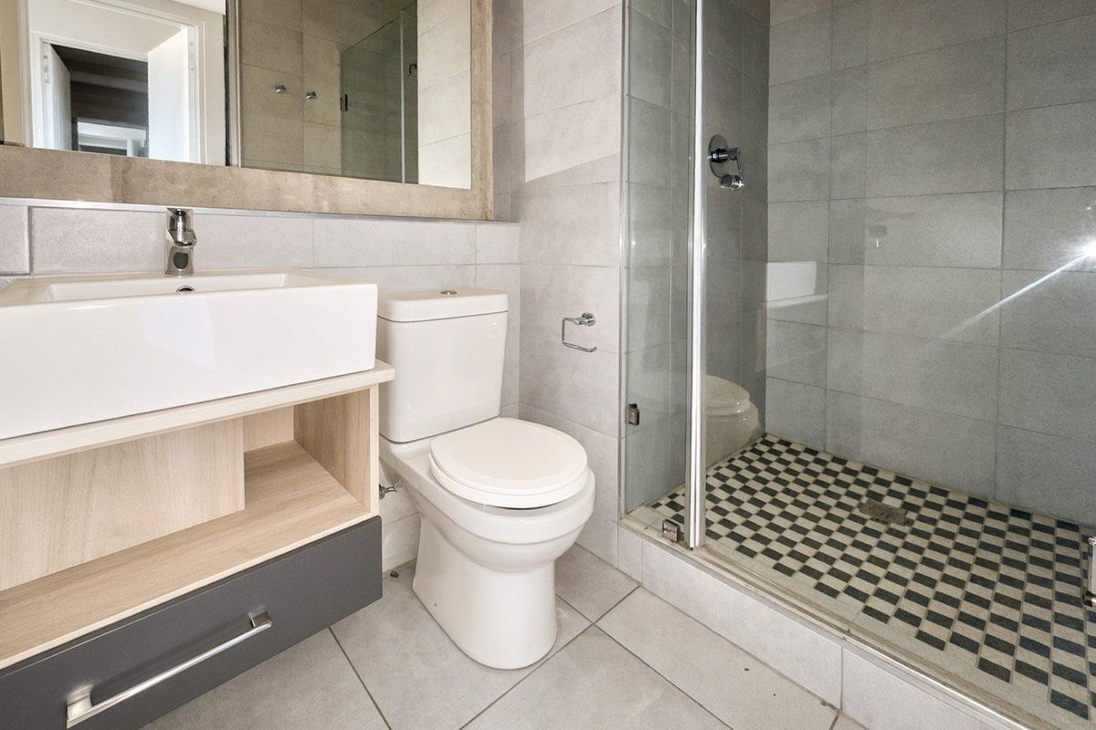 Modern bathroom featuring a vanity with basin, a toilet, and a glass-enclosed shower with decorative tiled flooring and neutral wall tiles.