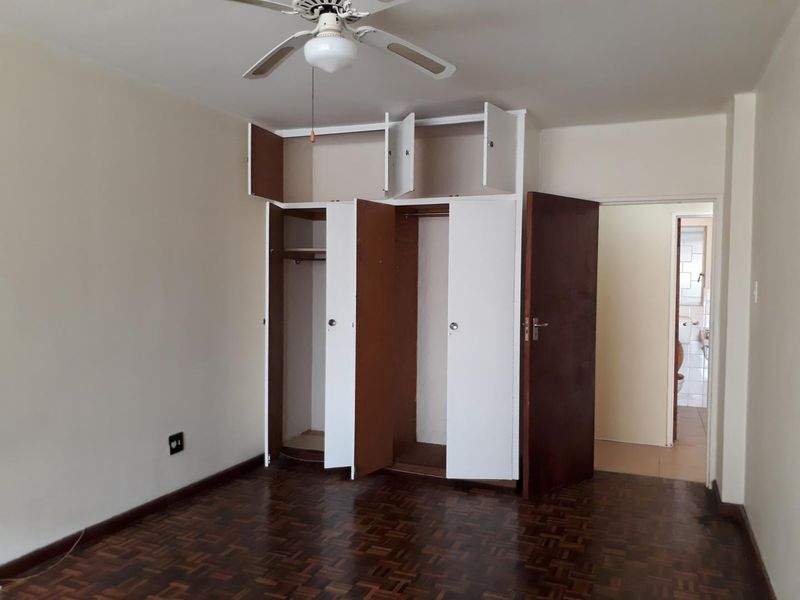 A bedroom featuring classic parquet flooring, a ceiling fan, and built-in storage cupboards, with an adjacent view into a bathroom area.