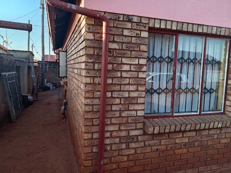 Side exterior view of the house featuring face brick walls, metal window security gates, and a downpipe system.
