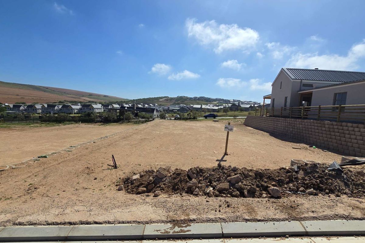 A vacant residential plot featuring a gentle slope, retaining wall, and expansive views of the surrounding estate and hills.