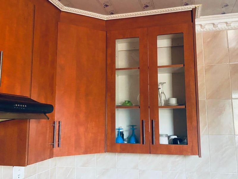 A close-up view of kitchen cabinetry featuring wooden cupboards, glass-fronted display units, an integrated extractor fan, and tiled wall finishes.