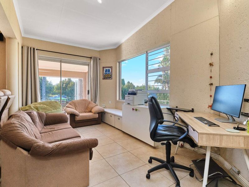 A multi-purpose living area featuring tiled flooring, built-in cabinetry, and large windows providing natural light and access to the outdoor patio area.