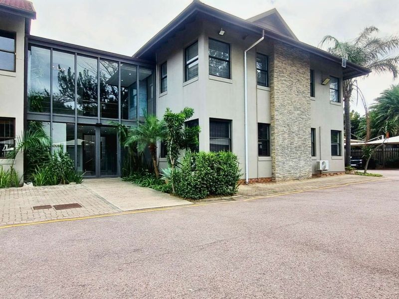 Modern office building exterior featuring a combination of stone cladding and a glass-fronted entrance lobby with paved driveway access.