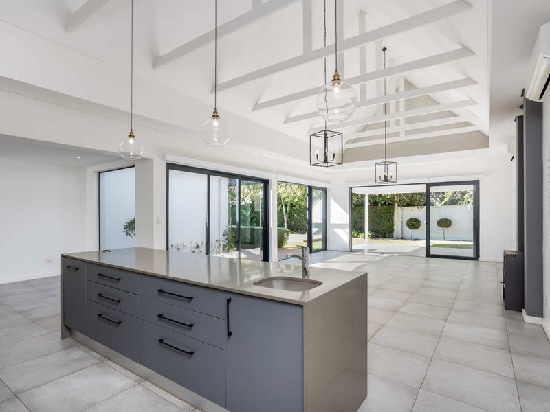 Spacious open-plan living area featuring a modern kitchen island, high vaulted ceilings with exposed rafters, and large sliding doors opening to the garden.