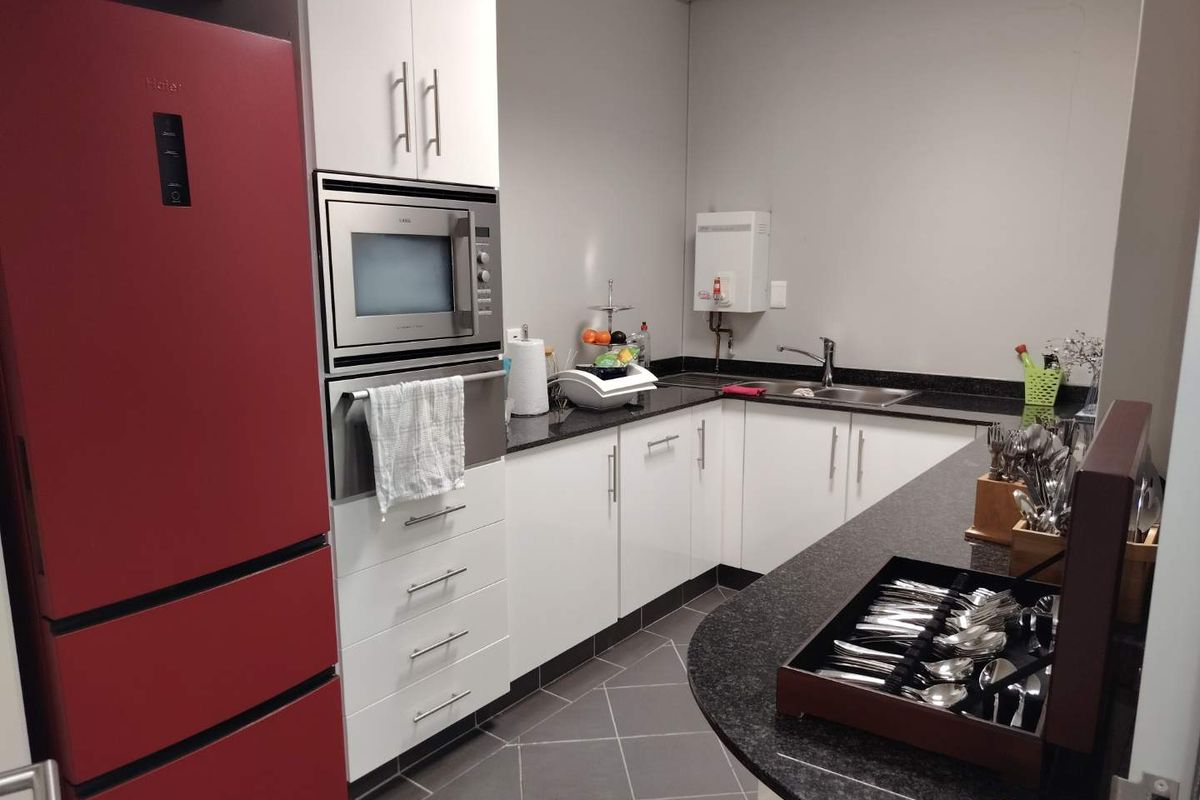 A compact office kitchenette featuring white cabinetry, dark granite countertops, a stainless steel built-in microwave, and a wall-mounted water heater.