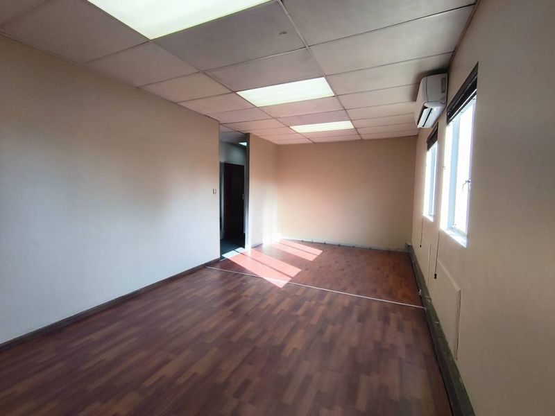 An empty office space featuring laminate flooring, a suspended ceiling with recessed lighting, and a wall-mounted air conditioning unit.