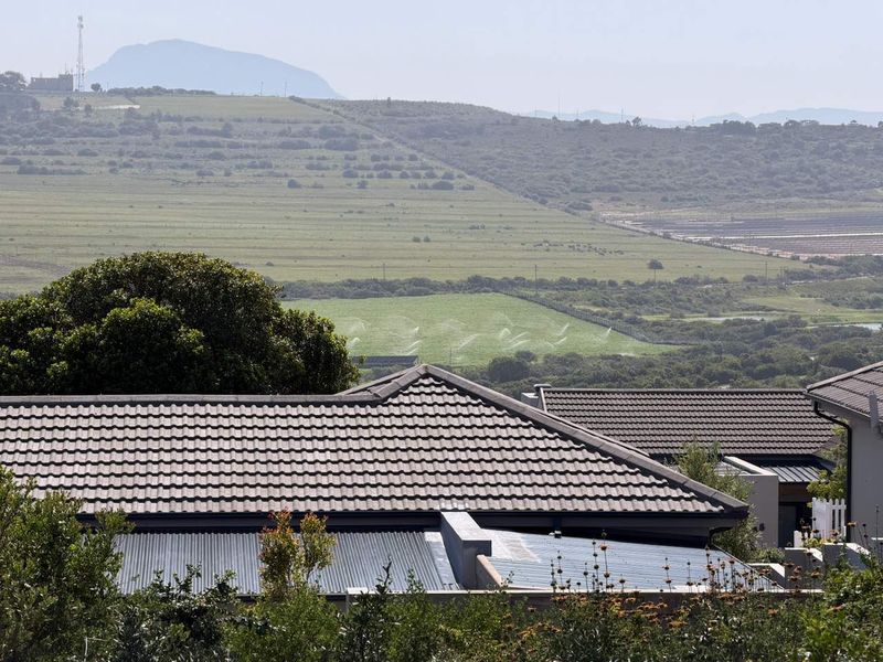 A scenic elevated view overlooking rolling green hills and agricultural land, framed by the tiled roofs of neighboring residential properties.