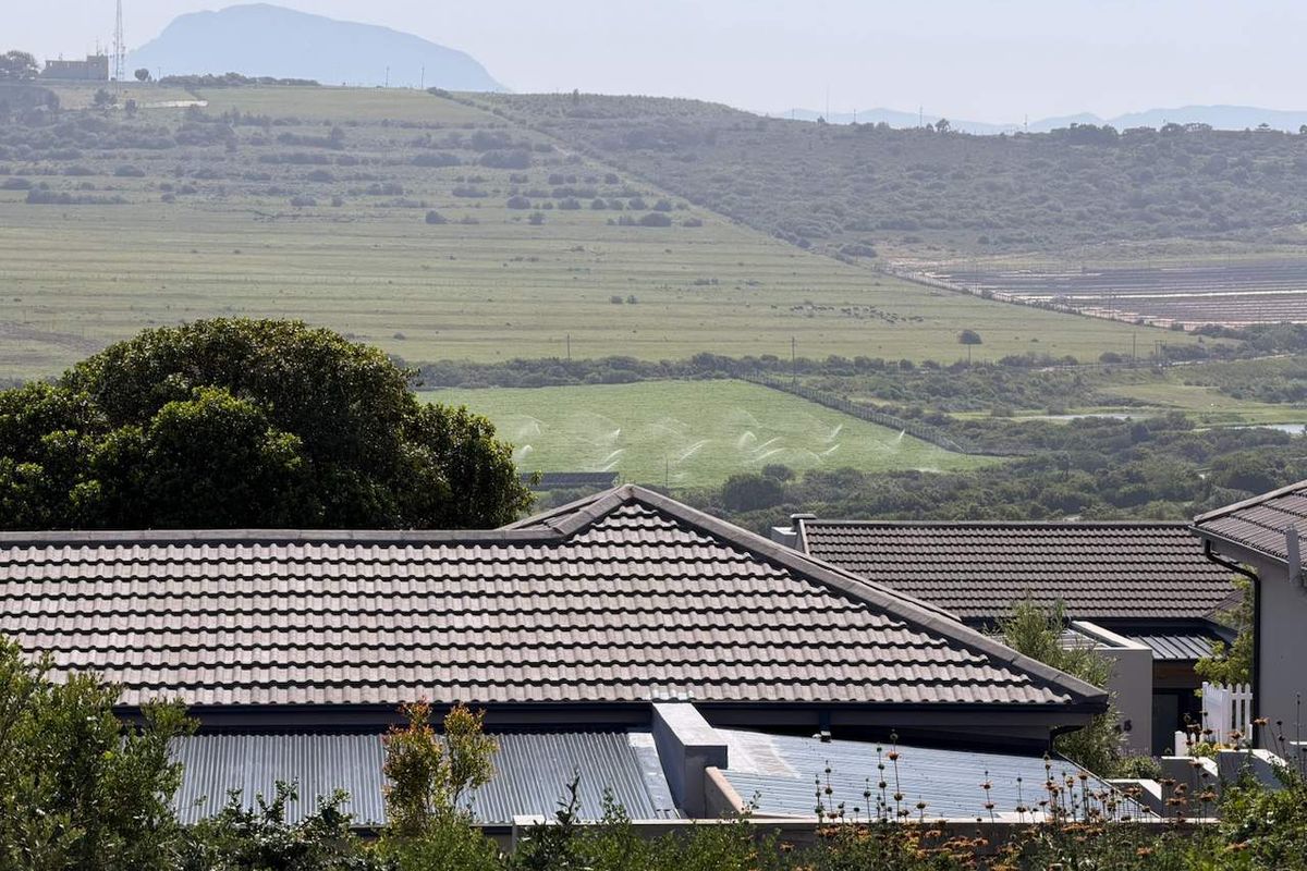 A scenic elevated view overlooking rolling green hills and agricultural land, framed by the tiled roofs of neighboring residential properties.