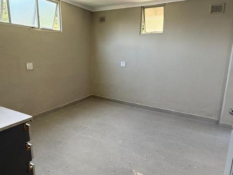 A bright, empty bedroom featuring neutral wall tones, polished tiled flooring, and multiple windows providing natural light.