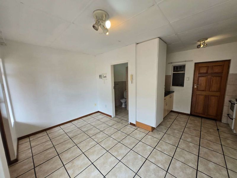 Open-plan living and kitchen area featuring tiled flooring, built-in cabinetry, and direct access to a bathroom, offering a functional blank canvas for renovation.