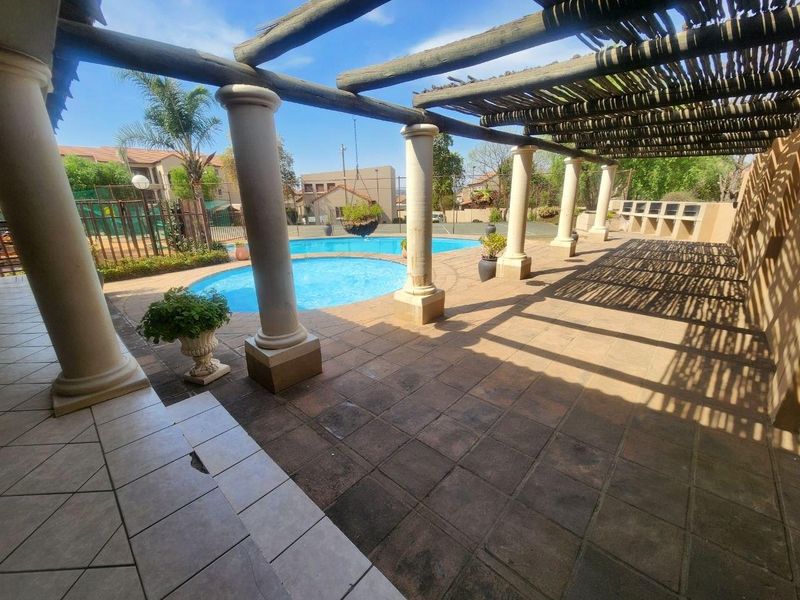 Outdoor entertainment area featuring a swimming pool, covered pergola with stone columns, and a built-in braai facility.
