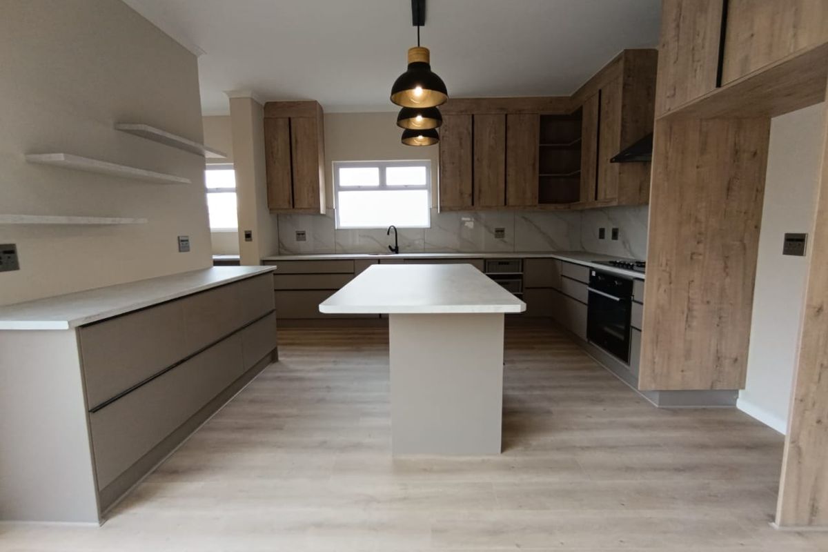 Modern kitchen featuring wood-grain cabinetry, a central island with stone countertop, built-in oven, gas hob, and sleek pendant lighting.