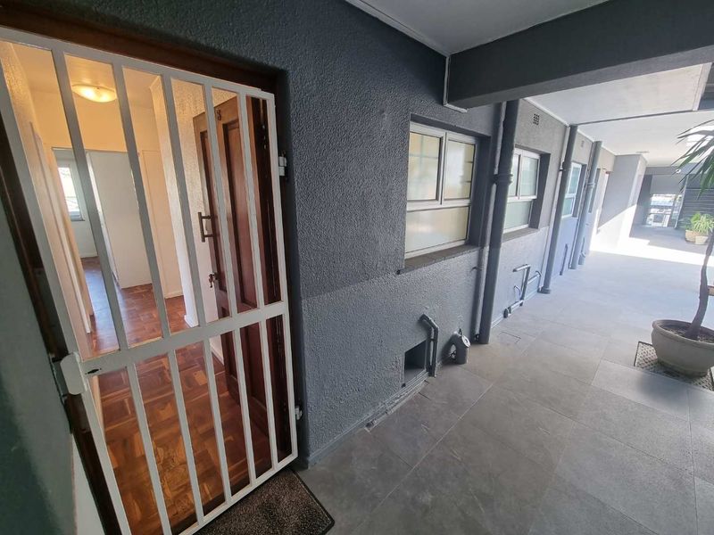 Apartment entrance featuring a secure metal gate, tiled walkway, and textured exterior wall finish with aluminium window frames.