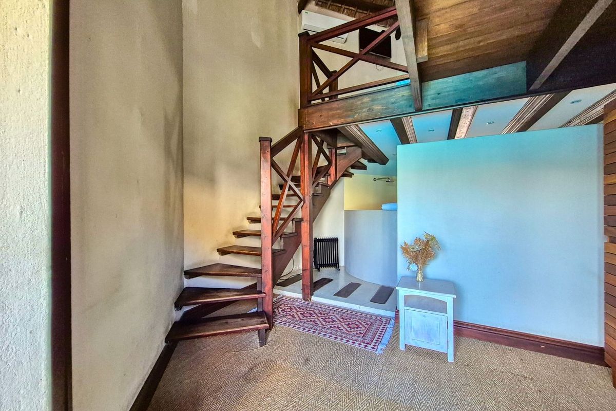 Living area featuring a wooden staircase leading to a mezzanine level with exposed timber beams and neutral wall finishes.