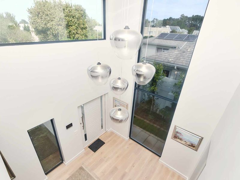 A bright, double-volume entrance hall featuring expansive floor-to-ceiling windows, modern timber flooring, and a contemporary front door.