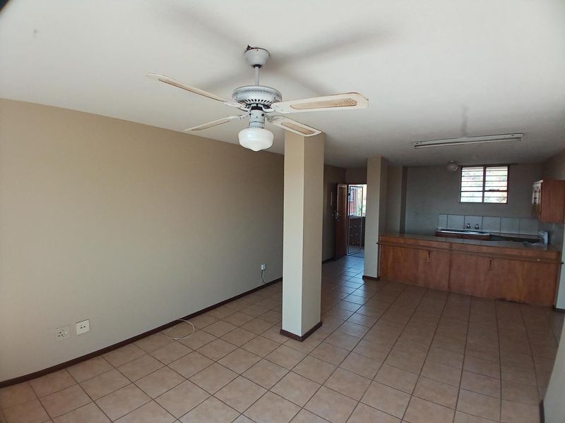 Open plan living and kitchen area featuring tiled flooring, a ceiling fan, and built-in wooden cabinetry with a breakfast counter.
