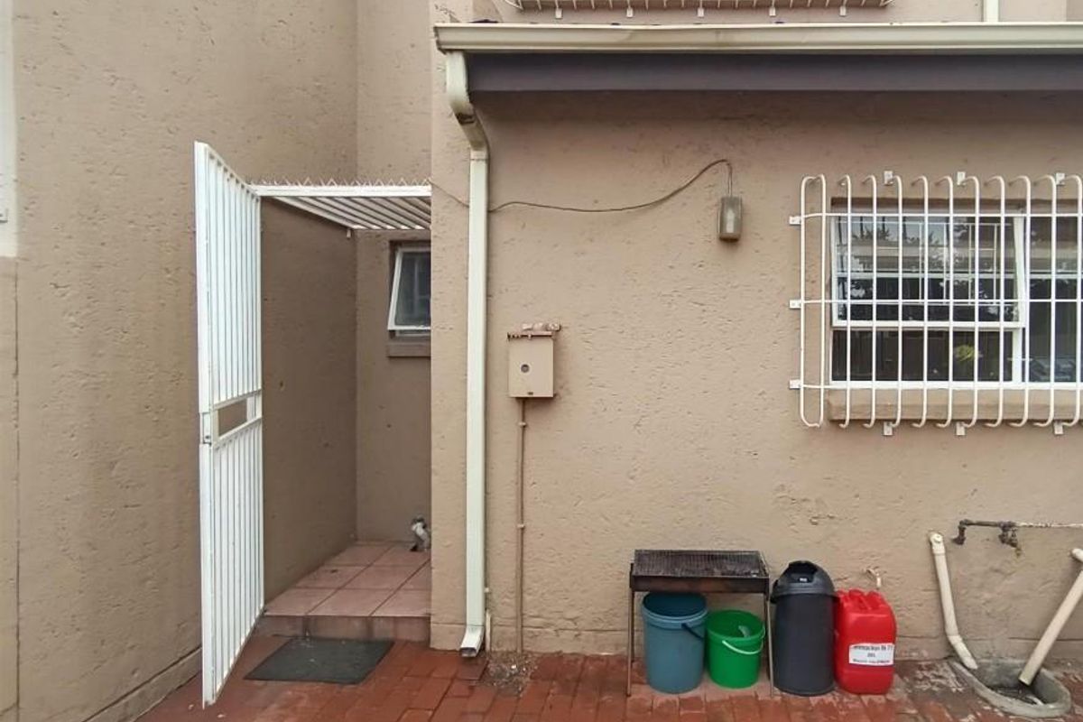 Rear exterior area of the townhouse featuring paved flooring, security gate, and security bars on the window.