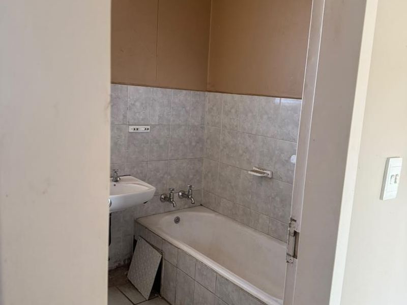 A dated bathroom featuring a bathtub and wall-mounted basin, requiring cosmetic updates and repairs to the tiling and wall finishes.