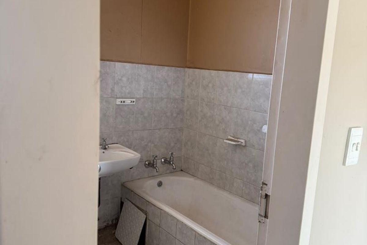 A dated bathroom featuring a bathtub and wall-mounted basin, requiring cosmetic updates and repairs to the tiling and wall finishes.