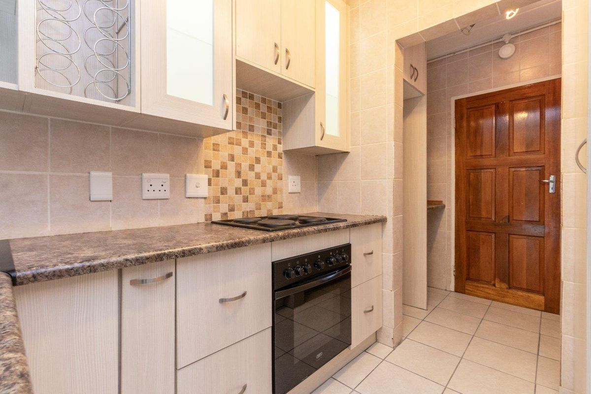 A functional kitchen featuring light-toned cabinetry, a tiled backsplash, built-in oven and hob, and tiled flooring, leading to a separate doorway.