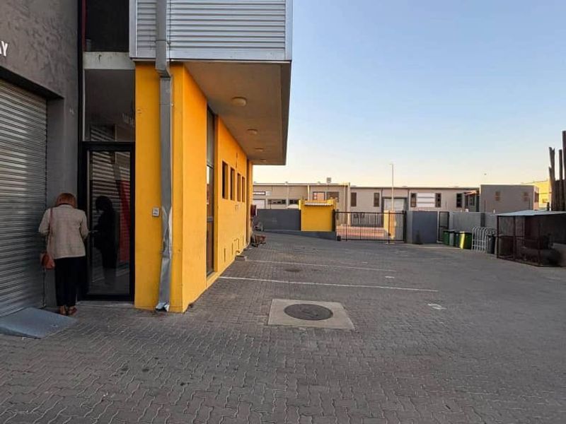 Industrial property exterior featuring a paved driveway, roller shutter door access, and yellow painted facade with metal cladding elements.