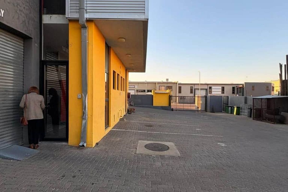 Industrial property exterior featuring a paved driveway, roller shutter door access, and yellow painted facade with metal cladding elements.