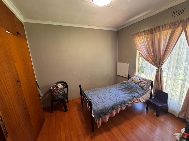 A functional bedroom featuring laminate flooring, a built-in wooden wardrobe, and a window with security bars, offering a blank canvas for potential updates.