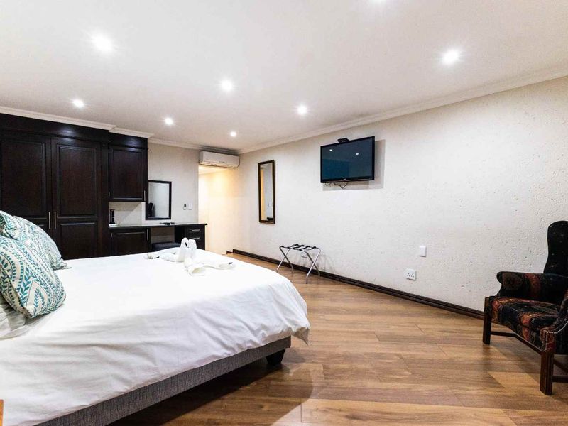 Spacious bedroom featuring dark wood built-in cabinetry, laminate flooring, recessed downlighting, and a wall-mounted air conditioning unit.